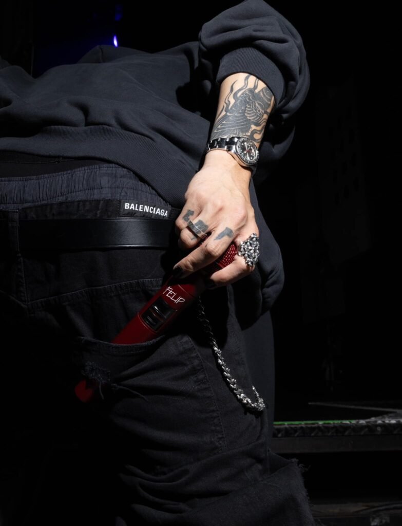 FELIP holding a red microphone with his hand and arm tattoos visible